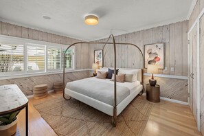 Relax in a serene bedroom with a four-poster bed, bedside tables, and a large window with horizontal blinds.