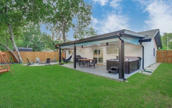 A backyard with a covered patio, a grill, and a hammock.