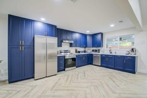 A modern kitchen with blue cabinets, stainless steel appliances, and a herringbone floor pattern.