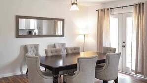A dining room with a dark wooden table and six upholstered chairs with button detailing. A floor lamp and a mirror are on the wall.