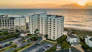 A high-rise hotel with multiple floors, a parking lot, and a view of the ocean at sunset. - Beachfront Getaway: Pool, Tennis & More! (Wrightsville Beach)