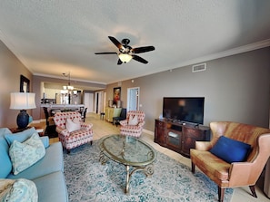 A living room with a ceiling fan, a television, patterned sofas, and a coffee table. - Windemere #1202 | Gulf Views + Pool & Hot Tub! (Perdido Key)