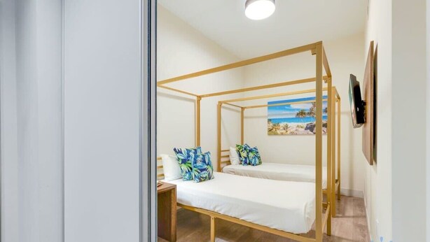 A room with a wooden four-poster bed, two pillows, a nightstand, and a painting of a beach scene.