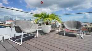A balcony with two wicker chairs, a potted plant, and a view of the cityscape.