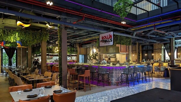 A modern restaurant with a bar area, high ceilings with exposed pipes, and a mix of seating arrangements.