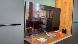 Cozinha moderna com TV embutida, bancada de madeira e uma pequena mesa com controle remoto e objetos decorativos.