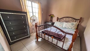 Ein Schlafzimmer mit Bett, Kommode und Standventilator.