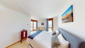 Une chambre d’hôtel avec un lit, une chaise, un bureau et une armoire. Elle dispose d’un balcon avec vue sur la ville.