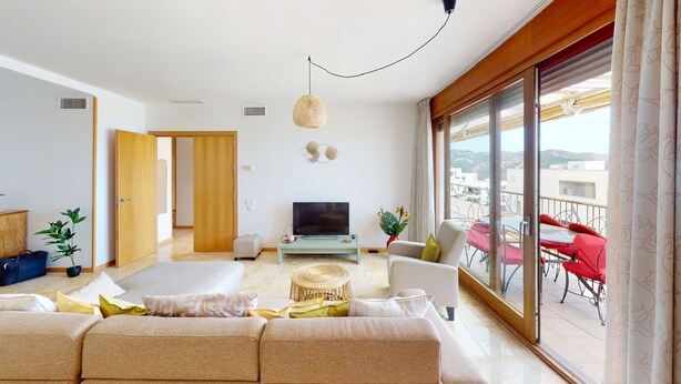 Un salon moderne avec un canapé, un téléviseur et un balcon agrémenté de chaises rouges.