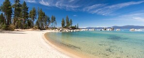 A beach with clear turquoise water, sandy shore, and tall pine trees. - 3BR Mountain Cabin-Near Beach & Slopes (Homewood)