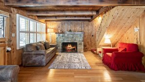 Interior acogedor de una cabaña con chimenea de piedra, paredes de madera, un sofá y un sillón rojo.