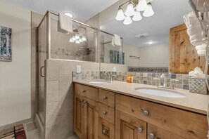 The downstairs shared bathroom is a spacious room with a large double-sink vanity, a stand-in shower with a glass door, and a jetted tub. - Ski-In/Ski-Out 3BR - Steps from Ski Resort! (Park City)