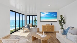 Ein geräumiges Wohnzimmer mit großem Fenster mit Meerblick, einem Holztisch und einer gemütlichen Sitzecke mit Sofa und Sesseln.