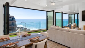 Ein modernes Wohnzimmer mit einem großen Glasfenster, das auf einen Balkon mit Blick aufs Meer führt.