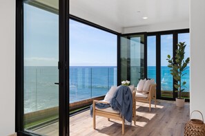 Un balcón con vista al mar, una silla con una manta y una planta en maceta.