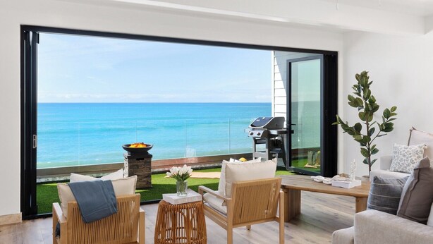 Ein modernes Wohnzimmer mit einem großen Glasfenster, das auf einen Balkon mit Meerblick führt.