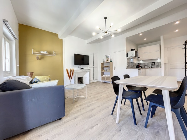 A modern living room with a sofa, a dining table with chairs, a TV, and a fireplace.