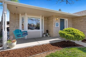 A house with a porch, a swing chair, a potted plant, and a well-maintained lawn.