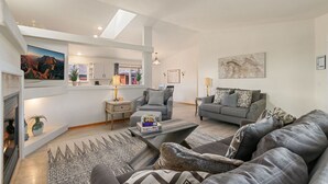 A modern living room with a fireplace, grey sofas, patterned rugs, and artwork on the walls. - Charming Home w/ RV Parking | 30 mi. from RMNP! (Loveland)