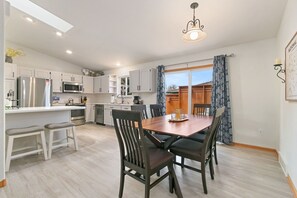 A modern kitchen with white cabinets, a stainless steel refrigerator, and a wooden dining table with chairs.