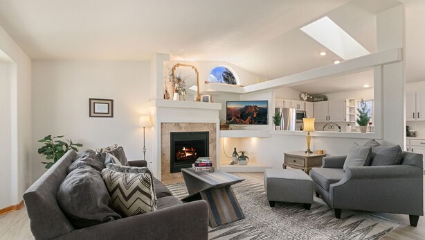 A modern living room with a fireplace, grey sofas, a coffee table, and a large TV. - Charming Home w/ RV Parking | 30 mi. from RMNP! (Loveland)