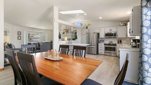 A modern kitchen with white cabinets, stainless steel appliances, and a dining area with a wooden table and chairs. - Charming Home w/ RV Parking | 30 mi. from RMNP! (Loveland)