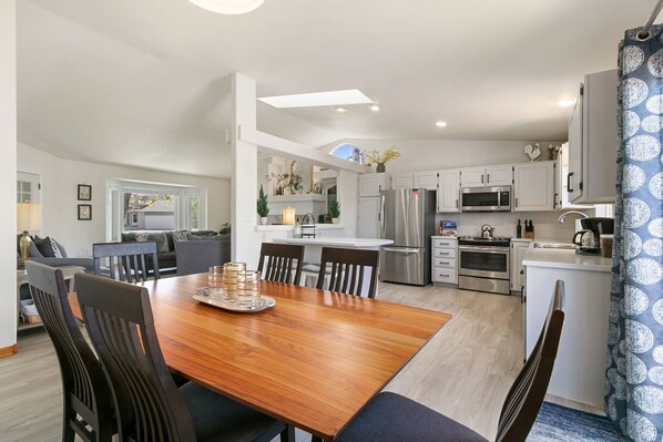 A modern kitchen with white cabinets, stainless steel appliances, and a dining area with a wooden table and chairs.