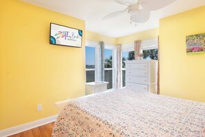 A bedroom with a bed, a dresser, a window with curtains, a ceiling fan, and a sign on the wall.