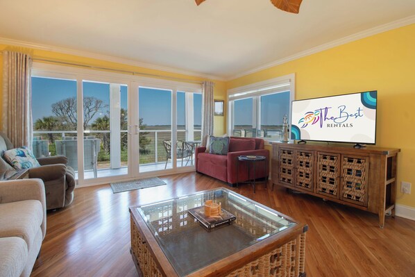 A spacious living room with a large glass coffee table, a red sofa, and a television on a wooden cabinet.