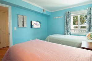 A bedroom with two beds, a window with curtains, a door, and a wall-mounted sign.