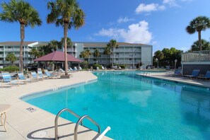 Piscina com espreguiçadeiras e palmeiras, ao redor de um edifício de hotel.