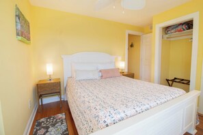 Um quarto com cama, duas mesas de cabeceira, um criado-mudo, uma porta e uma estante fixada na parede.