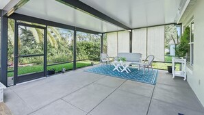 Un patio cubierto con un conjunto de asientos, ventanas amplias y vistas a la vegetación.