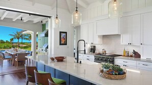 Une cuisine spacieuse avec des meubles blancs, un grand îlot central et des luminaires suspendus.
