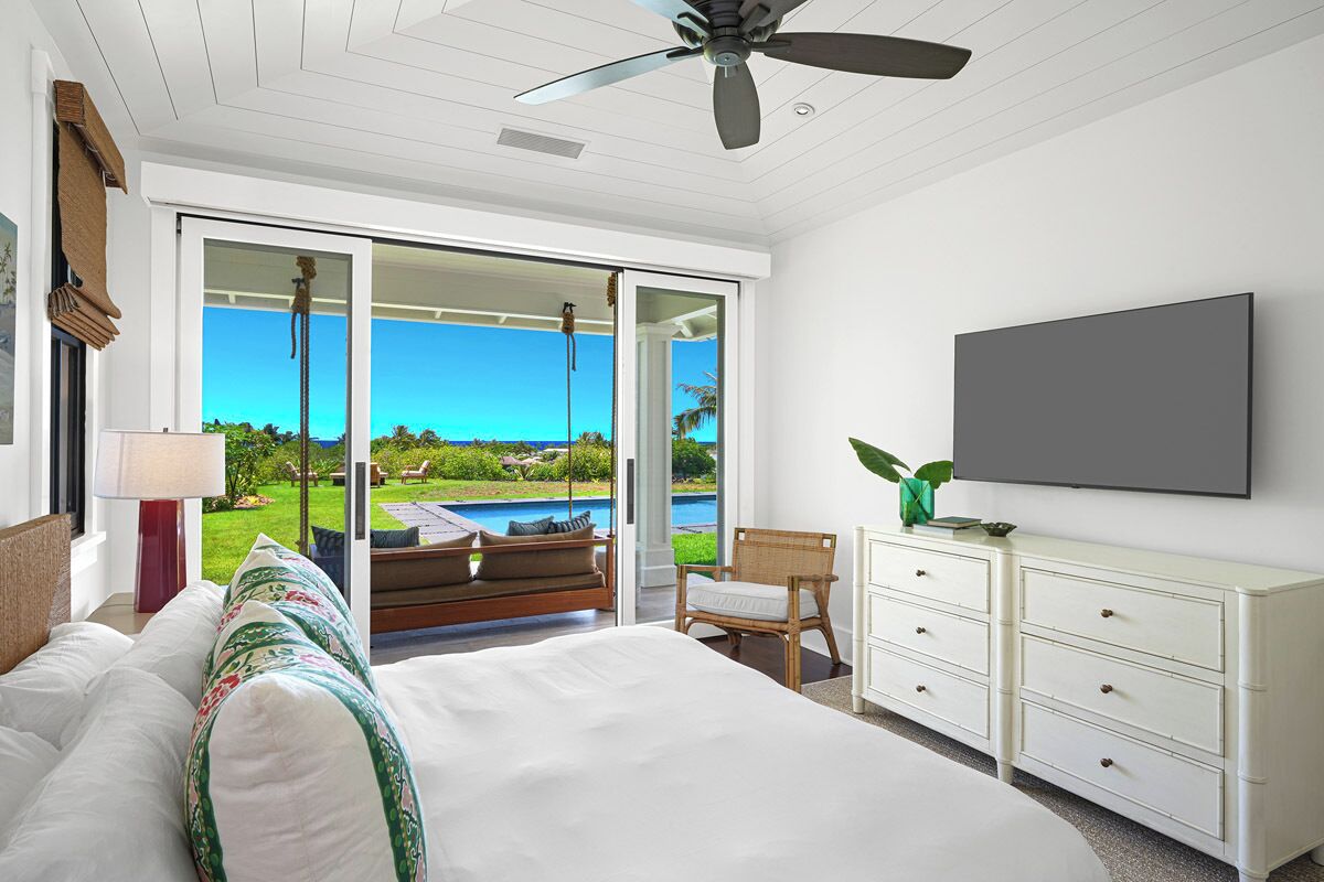 A bedroom with a large bed, a chair, a TV, and a view of a pool and greenery.