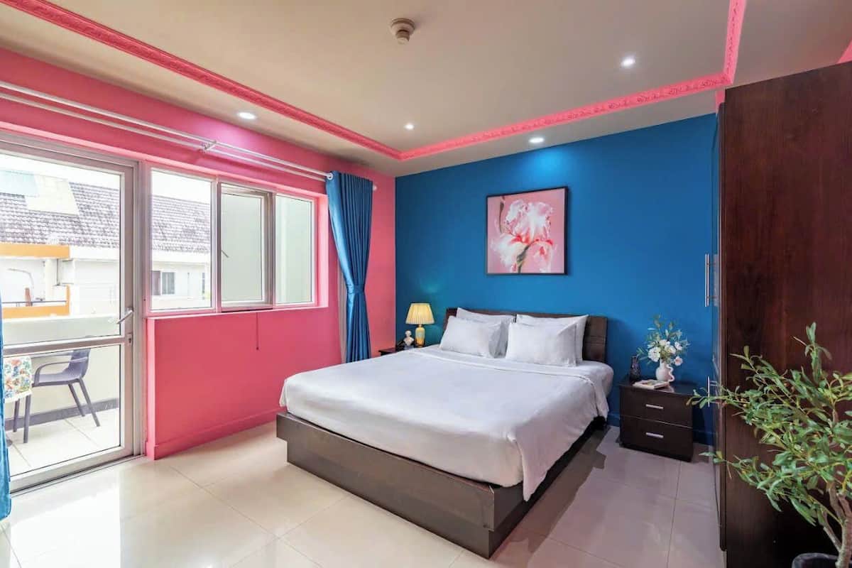 A bedroom with a bed, a nightstand, a lamp, a painting, and a potted plant.