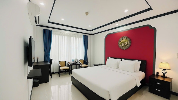 A hotel room with a large bed, a desk with two chairs, a TV, and a nightstand with a lamp. - La Serena Hotel & Apartment (Ho Chi Minh City)