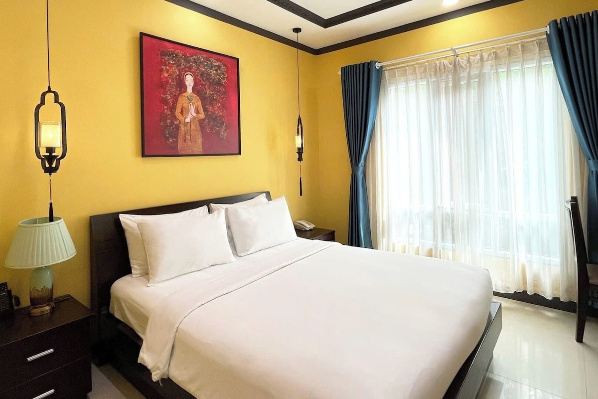 A hotel room with a bed, bedside table, lamp, and a painting on the wall.