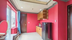A kitchen with red walls, a black refrigerator, wooden cabinets, and a window with a curtain. - La Serena Hotel & Apartment (Ho Chi Minh City)