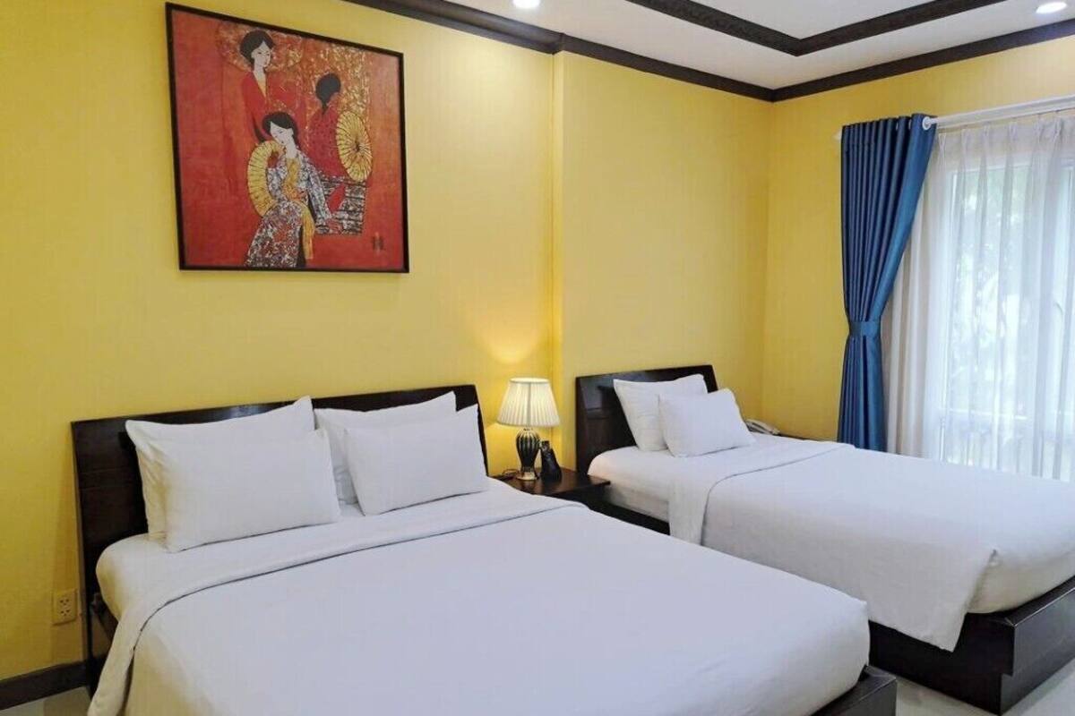 A hotel room with two beds, a painting on the wall, a nightstand with a lamp, and a window with curtains.