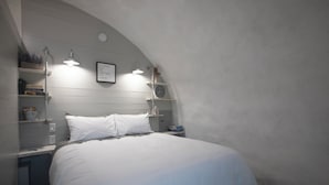 A bedroom with a bed, bedside tables, a wall clock, shelves with books and decorative items, and a ceiling light fixture. - Country Dome Suites (Bellville)