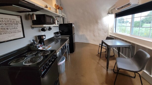 A compact kitchen with a stove, microwave, and sink, a small dining table with chairs, and a window providing a view of greenery outside. - Country Dome Suites (Bellville)