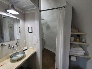 A bathroom with a sink, mirror, shower curtain, and shelves with towels. - Country Dome Suites (Bellville)