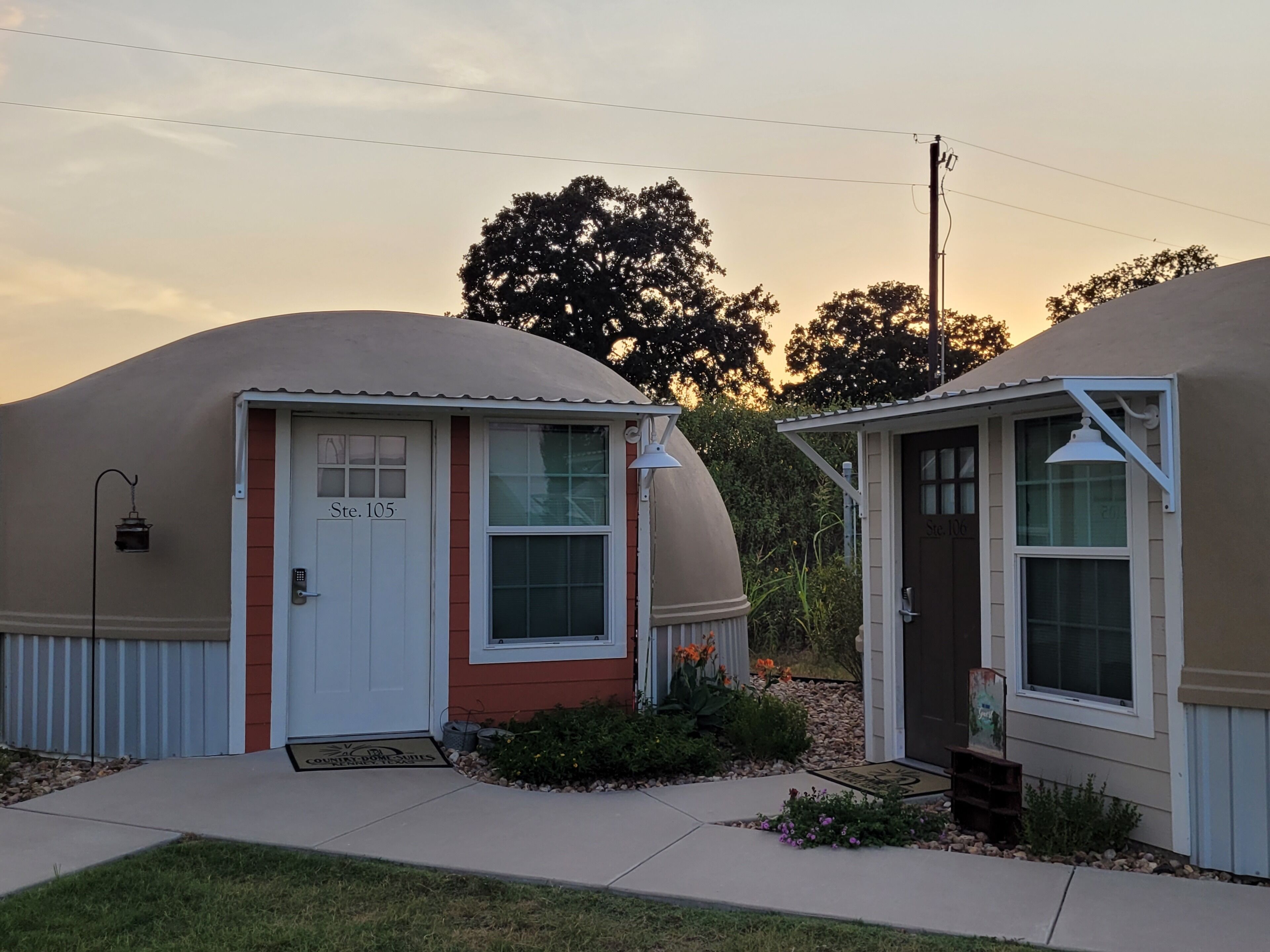 Two dome-shaped buildings with numbered doors, a small garden area, and a clear sky.