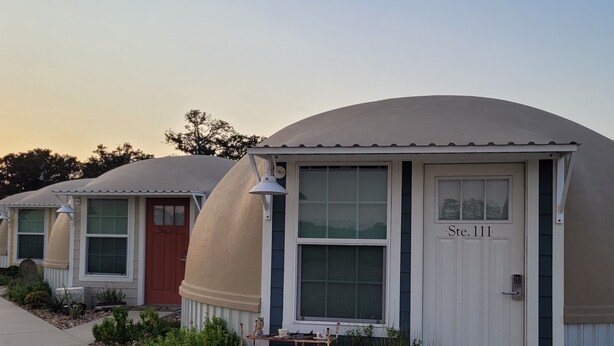 A row of dome-shaped mobile homes with numbered doors, a small garden area with plants, and a clear sky.