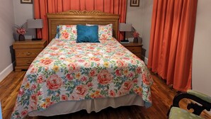 A bedroom with a floral bedspread, wooden headboard, two bedside tables with lamps, and matching curtains. - Little Blue Farmhouse (Jonesville)
