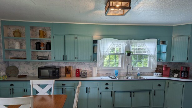 A kitchen with teal cabinets, a wooden dining table, and a white stove. - Little Blue Farmhouse (Jonesville)