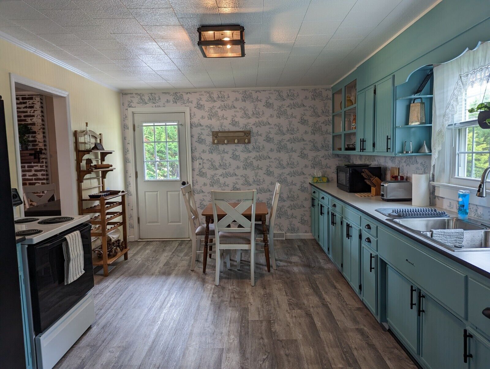 Una cocina con gabinetes color turquesa, una mesa de comedor de madera y una pared de ladrillo.