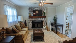 A living room with a fireplace, a sofa, a coffee table, and a dining area. - Little Blue Farmhouse (Jonesville)
