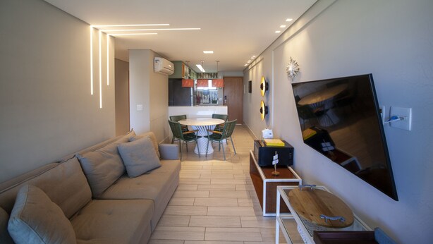 Un soggiorno moderno con un divano, un tavolo da pranzo con sedie, una TV a parete e una cucina sullo sfondo.